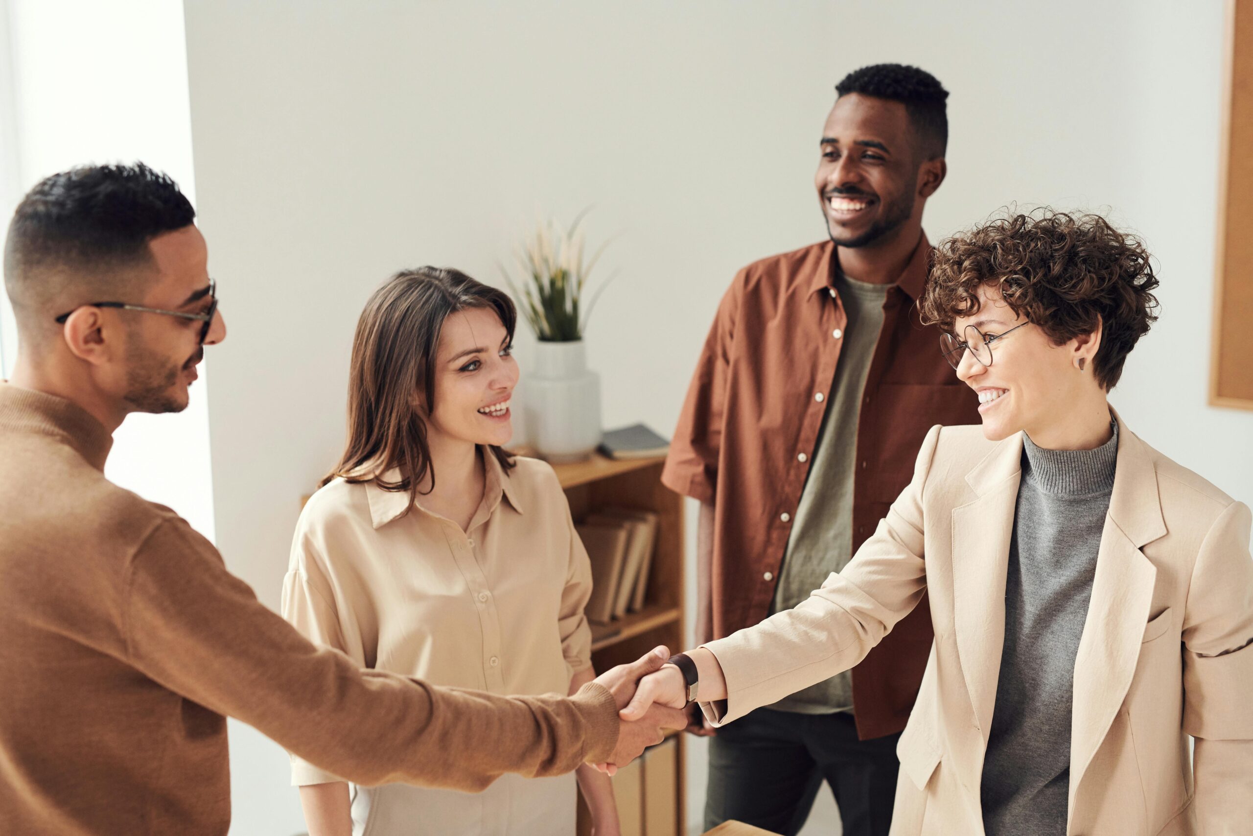 Home Four colleagues smiling and shaking hands in a bright office setting.