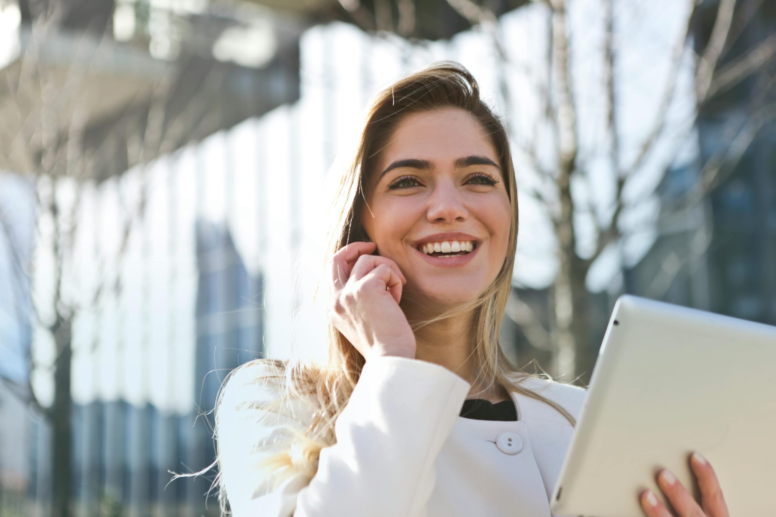 Home Confident businesswoman using her tablet and phone, smiling outdoors in sunlight.